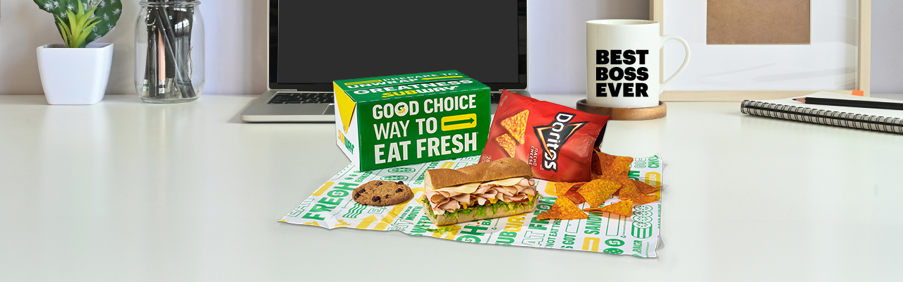 A Subway® Catering lunch box on a desk in front of a laptop and Best Boss Ever mug.